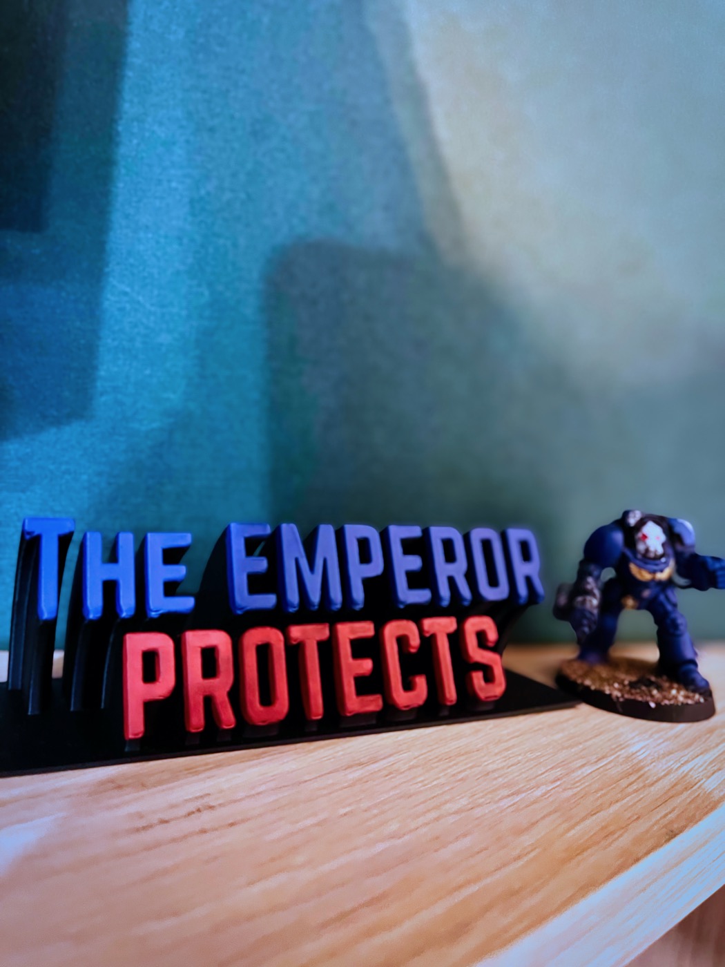 Tischschild „The Emperor Protects“ neben einer bemalten Miniatur